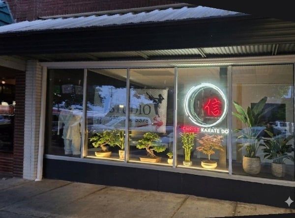 Karate dojo storefront at night with red neon sign, illuminated plants, and glass windows displaying interior